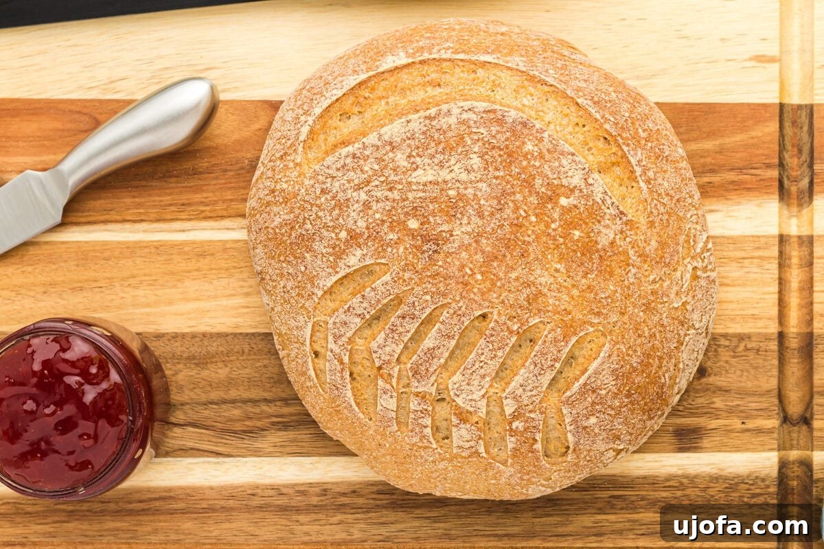 The Art of Gluten-Free Sourdough 14 A freshly baked, golden brown boule of gluten-free sourdough bread on a wooden cutting board, with a knife and jam, ready to be enjoyed.