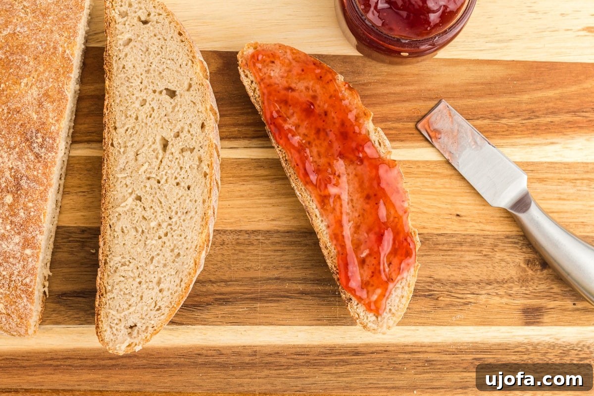 The Art of Gluten-Free Sourdough 15 Several slices of perfectly baked gluten-free sourdough bread arranged on a wooden cutting board, alongside a knife and a small bowl of jam.