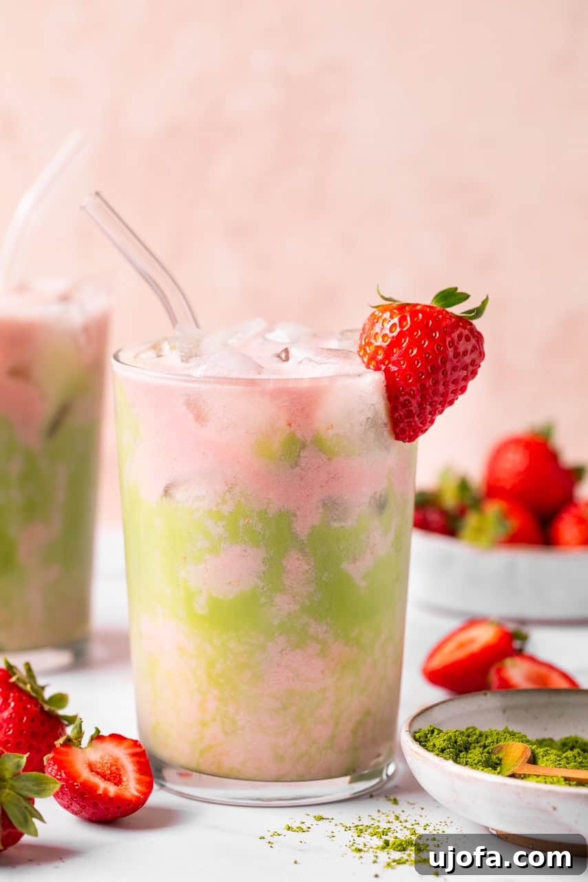 A close-up view of an iced matcha strawberry tea latte in a glass, featuring a straw and a strawberry garnish, highlighting the beautiful texture and colors.