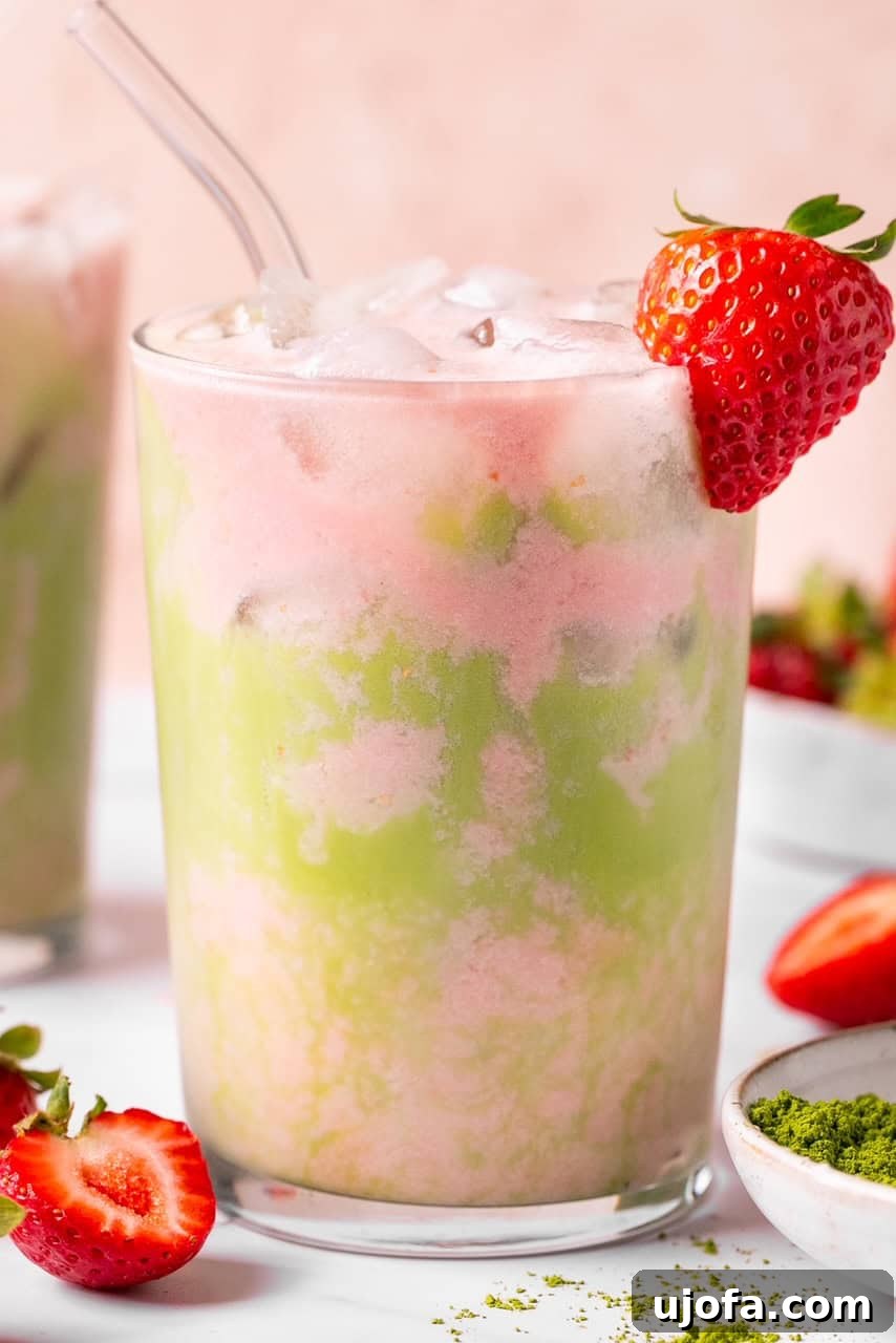 An iced matcha strawberry latte in a glass with ice, viewed from an angle to show the drink's layers.