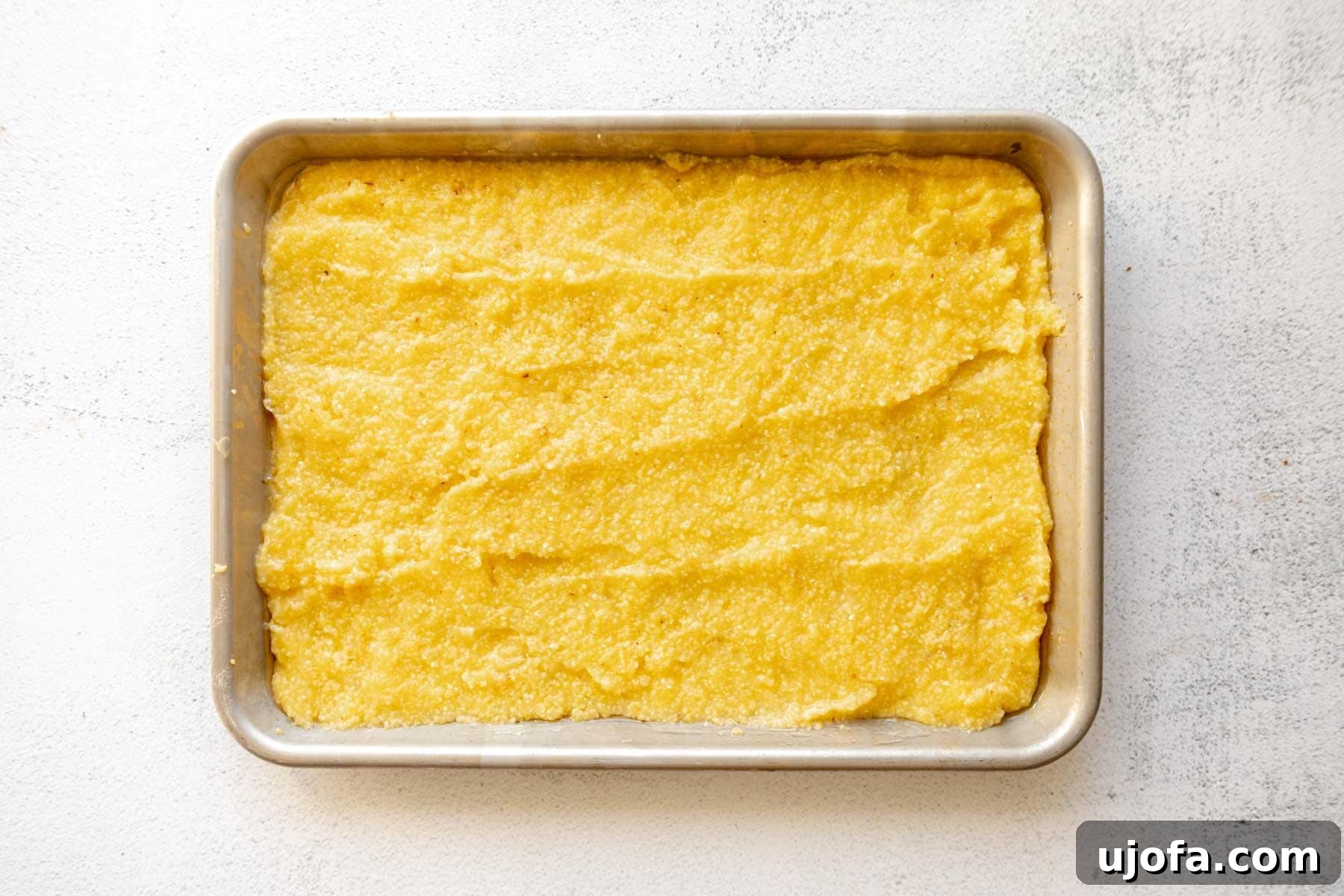 Golden Fried Grits 7 Cooked grits evenly spread out on a greased baking sheet, preparing for chilling.