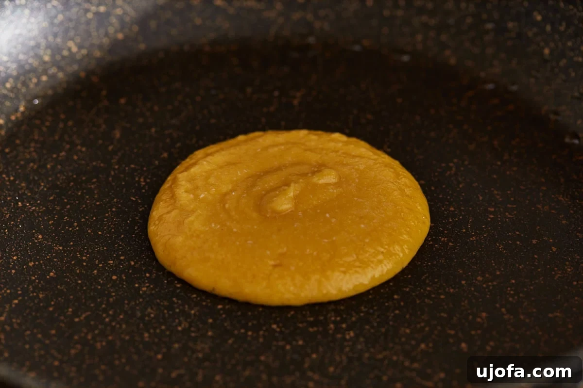 A dollop of coconut flour pancake batter cooking on a lightly greased griddle over medium heat, starting to bubble.
