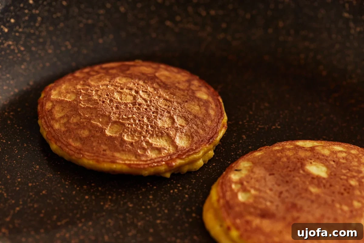 Multiple coconut flour pancakes cooking simultaneously on a griddle, some flipped to a golden brown and others still cooking.
