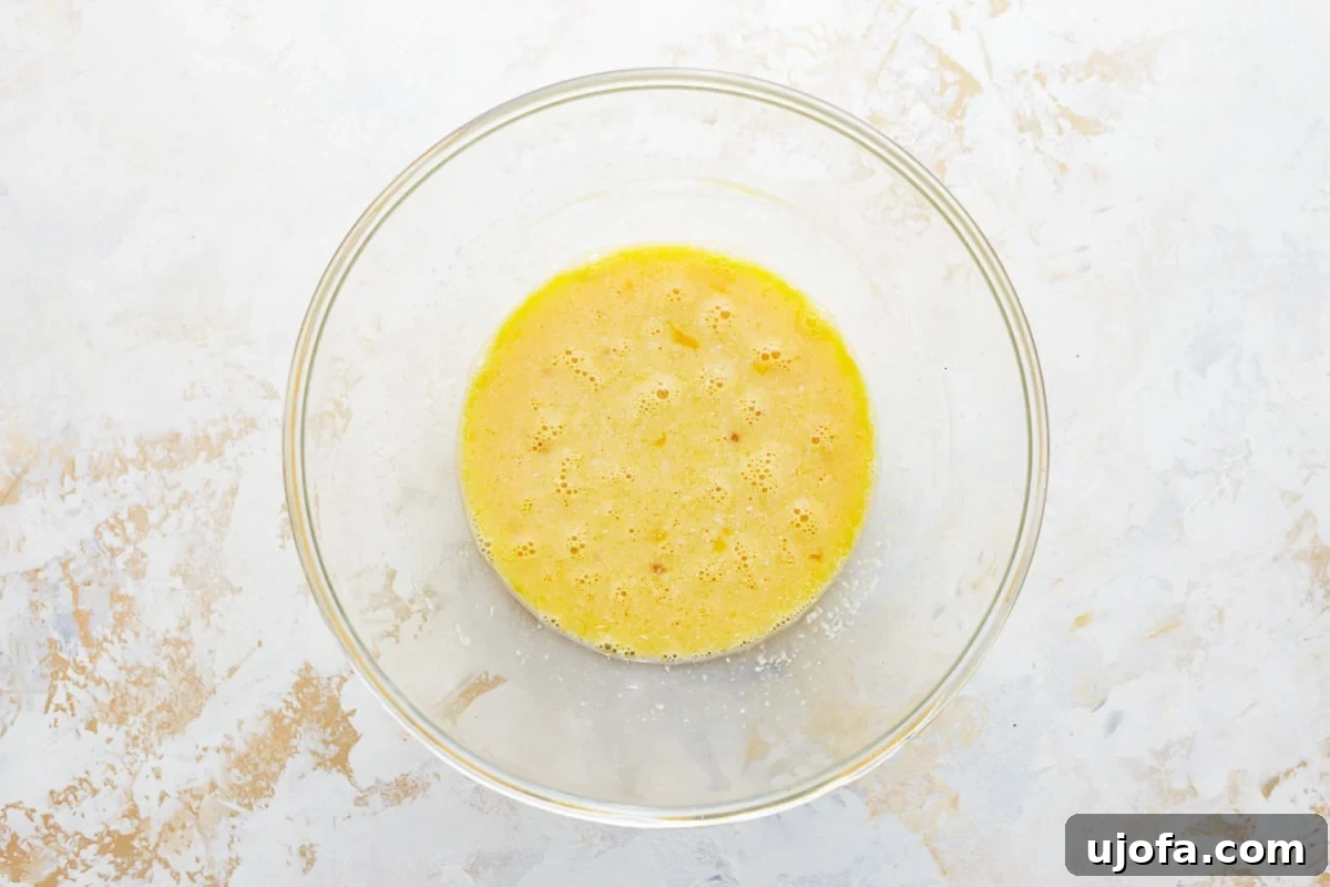 Whisked eggs in a separate glass bowl, mixed with other wet ingredients like almond milk, coconut oil, maple syrup, and vanilla extract.