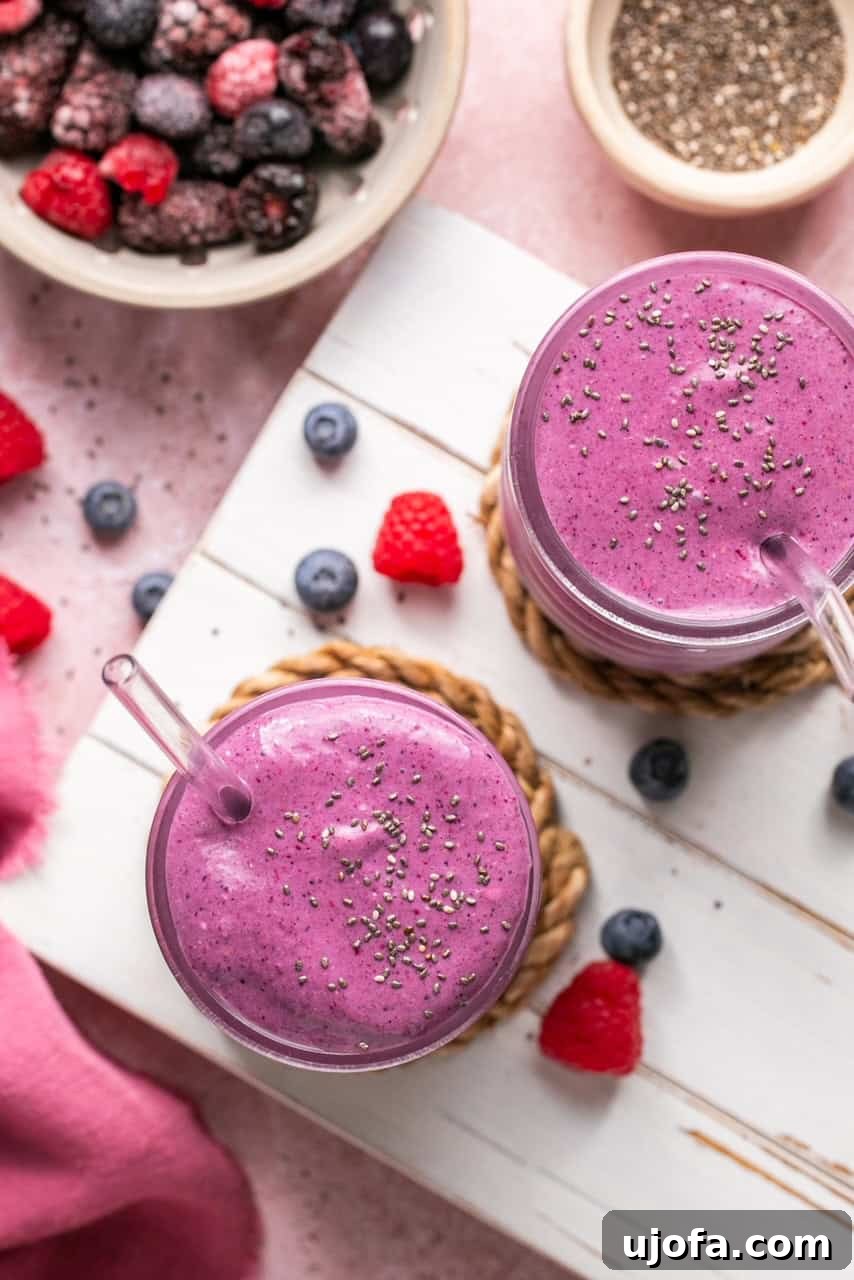 An overhead shot of two vibrant berry cheesecake cottage cheese smoothies, artfully topped with chia seeds, in tall glasses with glass straws.