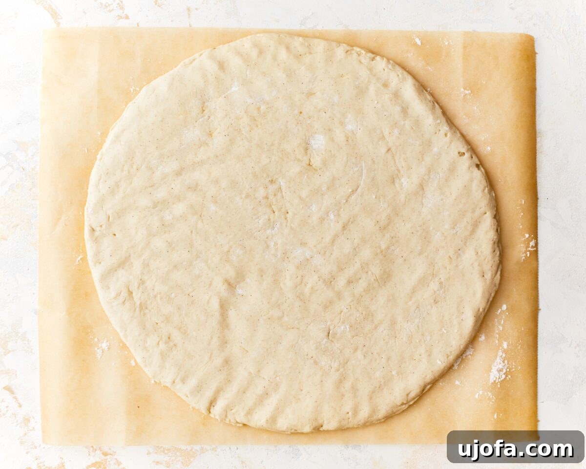 Gluten-free pizza dough shaped into a perfect 15-inch circle on floured parchment paper, with a defined crust edge, ready for its first bake.