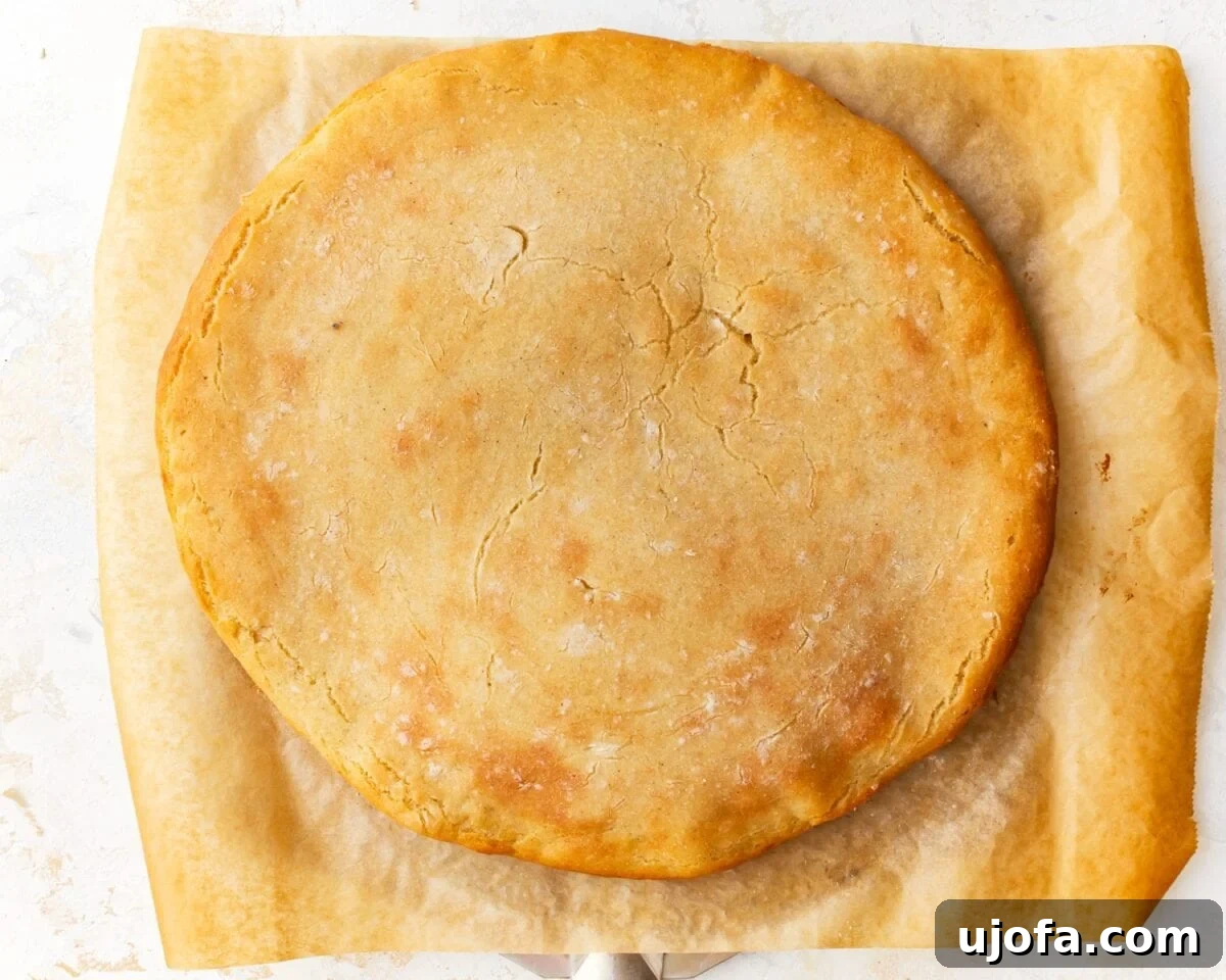 A baked gluten-free pizza crust on parchment paper, golden and firm, ready for toppings, showcasing its sturdy base.