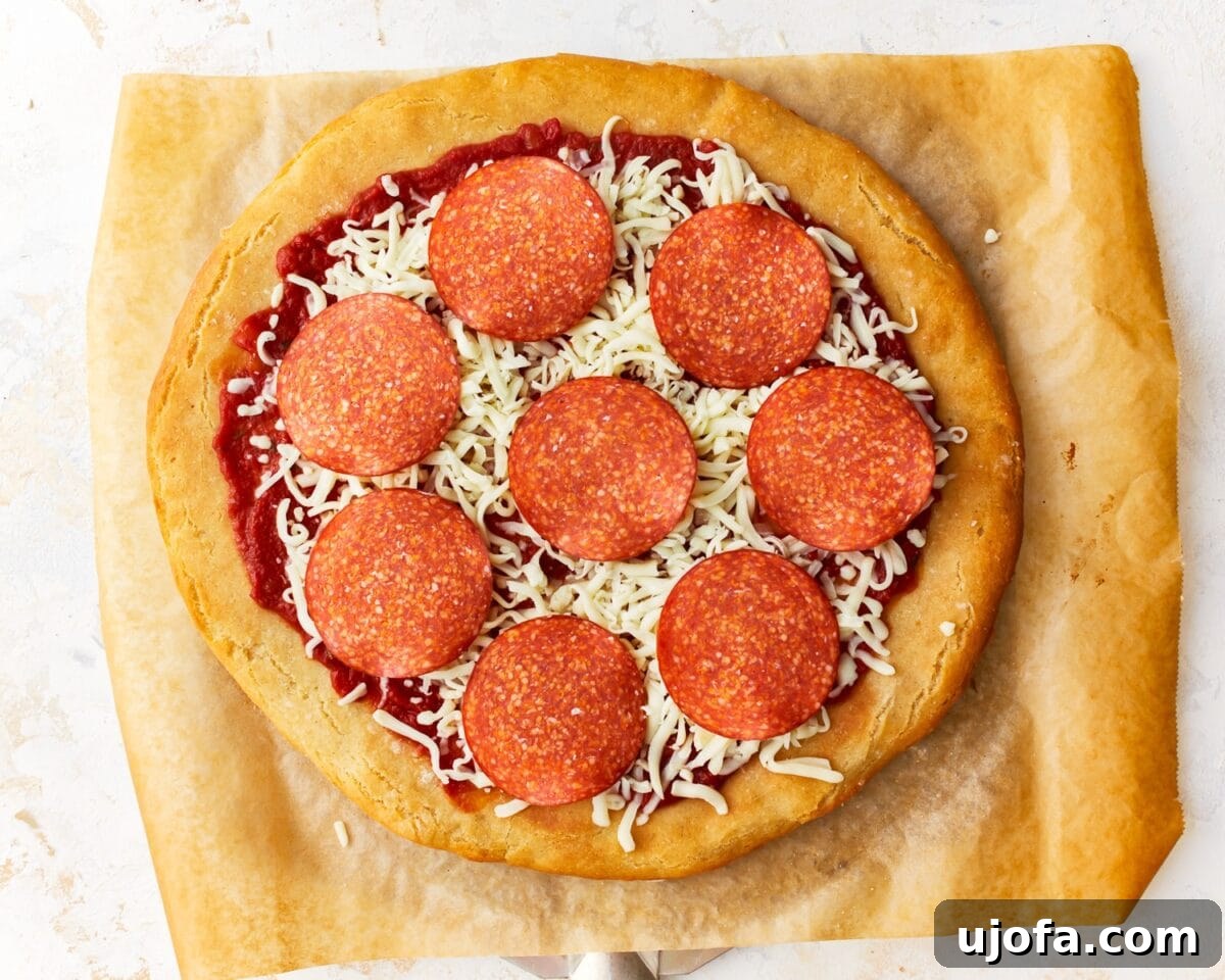 A partially assembled gluten-free pepperoni pizza with vibrant tomato sauce, generous shredded mozzarella, and perfectly spaced pepperoni slices on a golden, baked crust, poised to go back into the oven for melting.