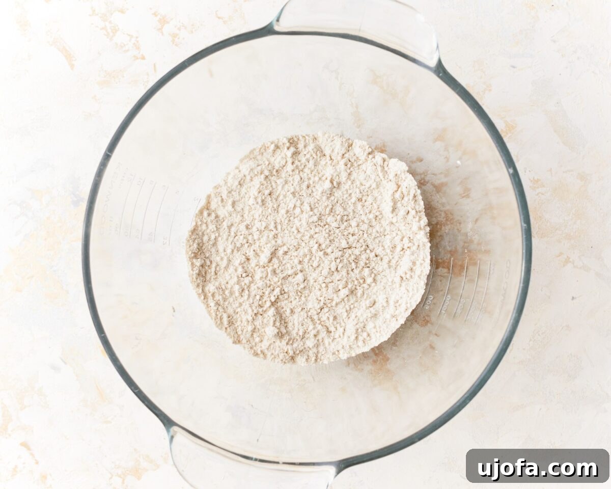 A glass mixing bowl filled with a dry mixture of gluten-free flour, yeast, baking powder, and salt, waiting for wet ingredients.