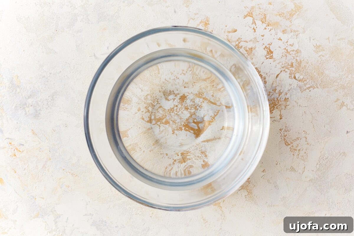 A clear glass bowl holding warm water, with a thermometer checking the temperature, signifying activated yeast.