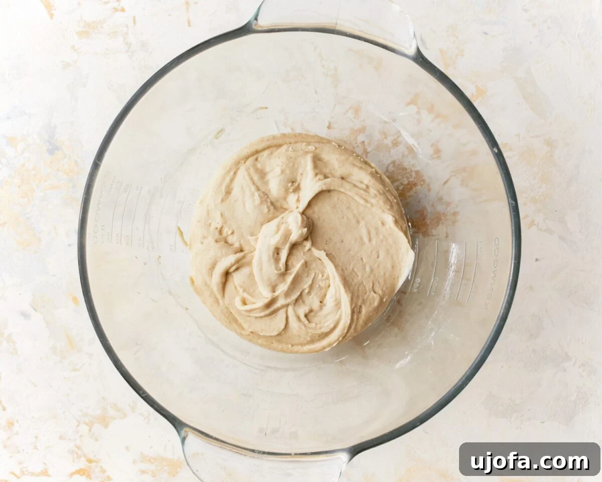 Gluten-free pizza dough just beginning to come together in a glass mixing bowl after mixing, showing a rough texture.
