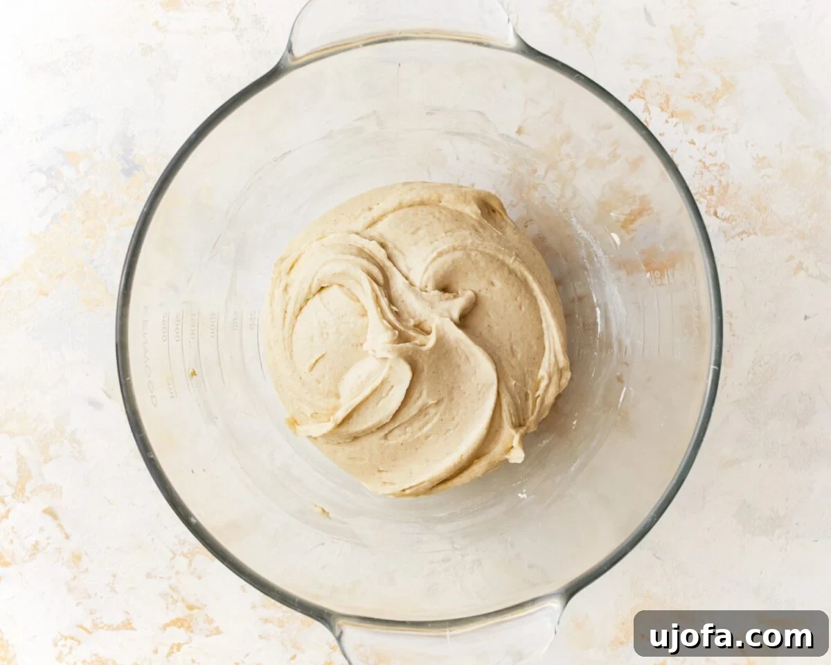 Gluten-free pizza dough fully mixed and slightly smoother in texture, resting in a glass mixing bowl, appearing sticky.