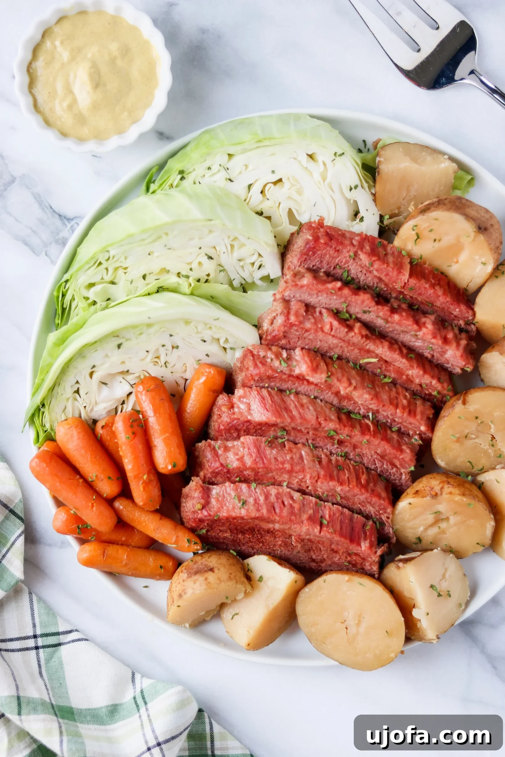 A close-up of thinly sliced corned beef served with tender cabbage wedges and a dollop of mustard.