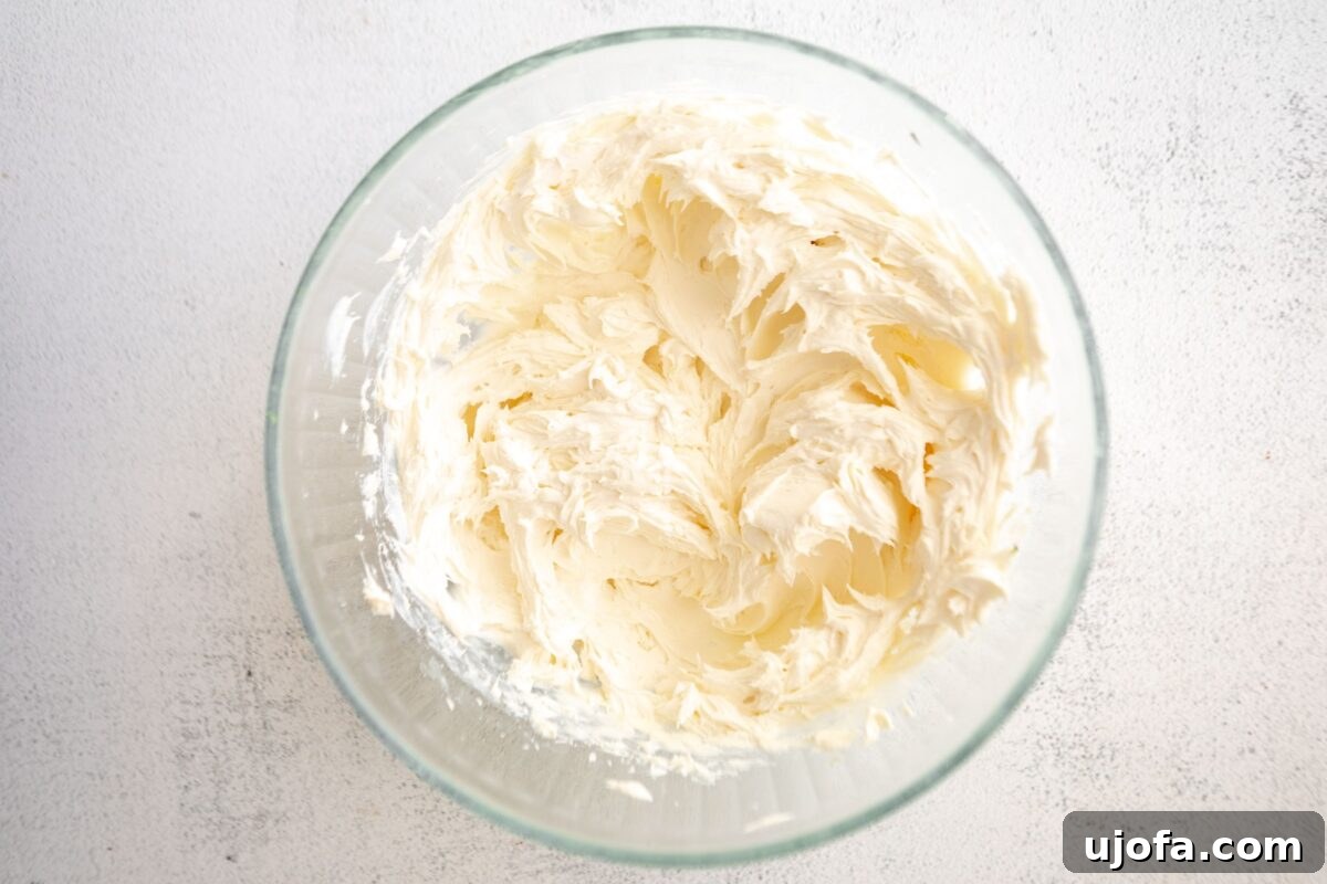 Silken Cheesecake 5 Whipped cream cheese mixture in a clear glass bowl, showing a fluffy, thick texture achieved after initial beating.