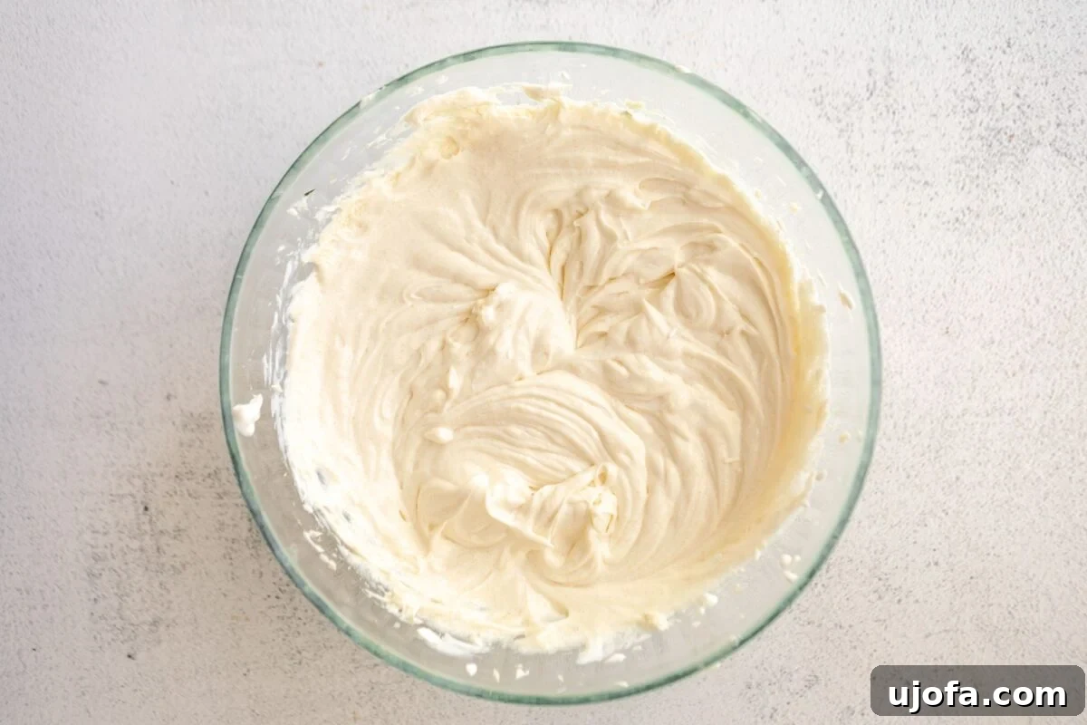 Silken Cheesecake 6 Smooth cheesecake batter after mixing in sugar, sour cream, and vanilla, presented in a clear glass mixing bowl, showcasing its consistent texture.