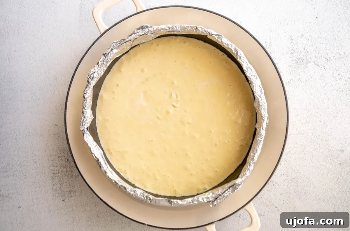 Silken Cheesecake 8 Cheesecake batter poured into a parchment and foil-lined springform pan, sitting within a larger pan, prepared for baking in a water bath.