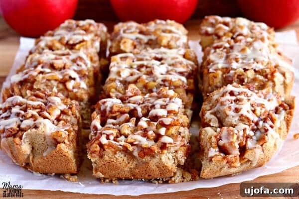 Nine perfectly cut gluten-free apple pie blondies arranged on white parchment paper, resting on a cutting board, with three vibrant red apples creating a beautiful backdrop.