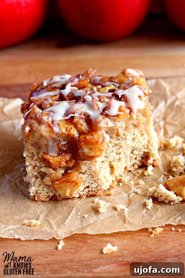 Close-up of a gluten-free apple pie blondie with a bite taken out, revealing its soft texture and apple filling, placed on parchment paper with red apples in the background.