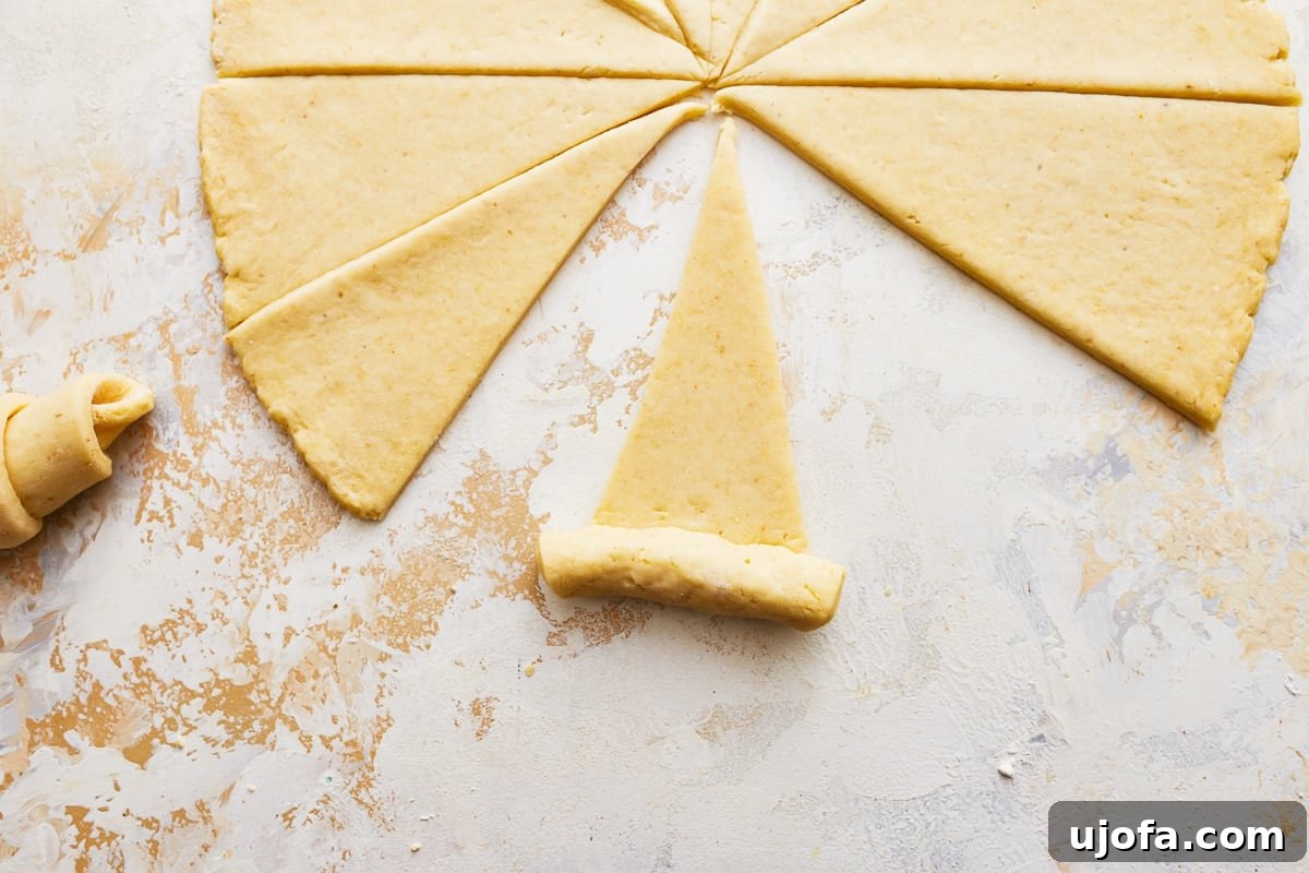 Buttery Gluten-Free Crescent Rolls 8 gluten-free crescent roll dough being shaped from a triangle on a floured surface.