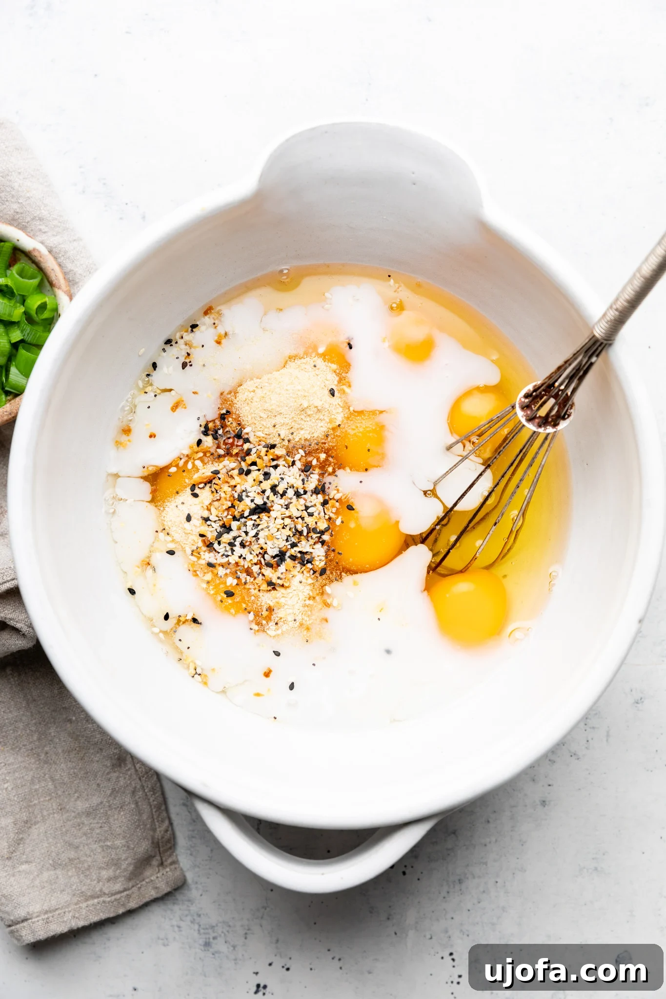Wholesome Breakfast Casserole Gluten Free Dairy Free 4 Eggs, dairy-free milk, and everything bagel seasoning ready to whisk in a white mixing bowl on a light colored surface.