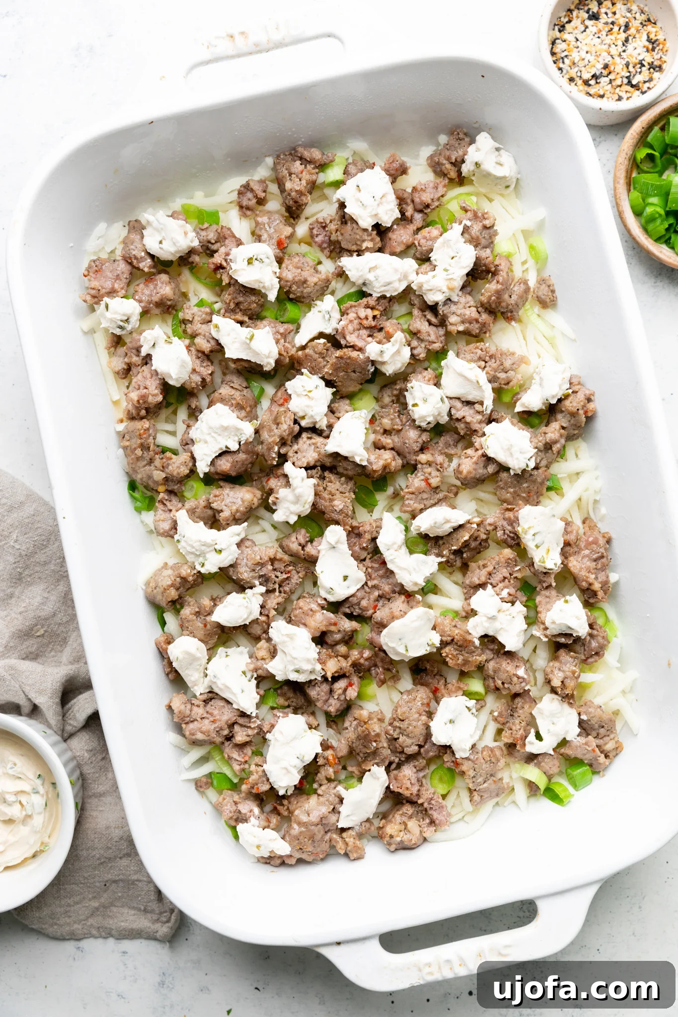 Wholesome Breakfast Casserole Gluten Free Dairy Free 5 Hash browns, cooked sausage, green onions, and dollops of dairy-free cream cheese layered in a white casserole dish.