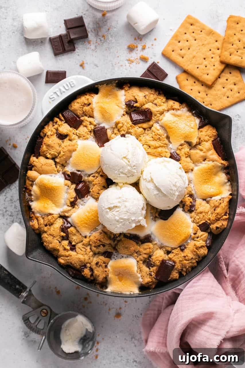 An overhead shot of a perfectly baked chocolate and marshmallow cookie skillet in a cast iron pan, still warm, with a scoop of vanilla ice cream gently melting on top.
