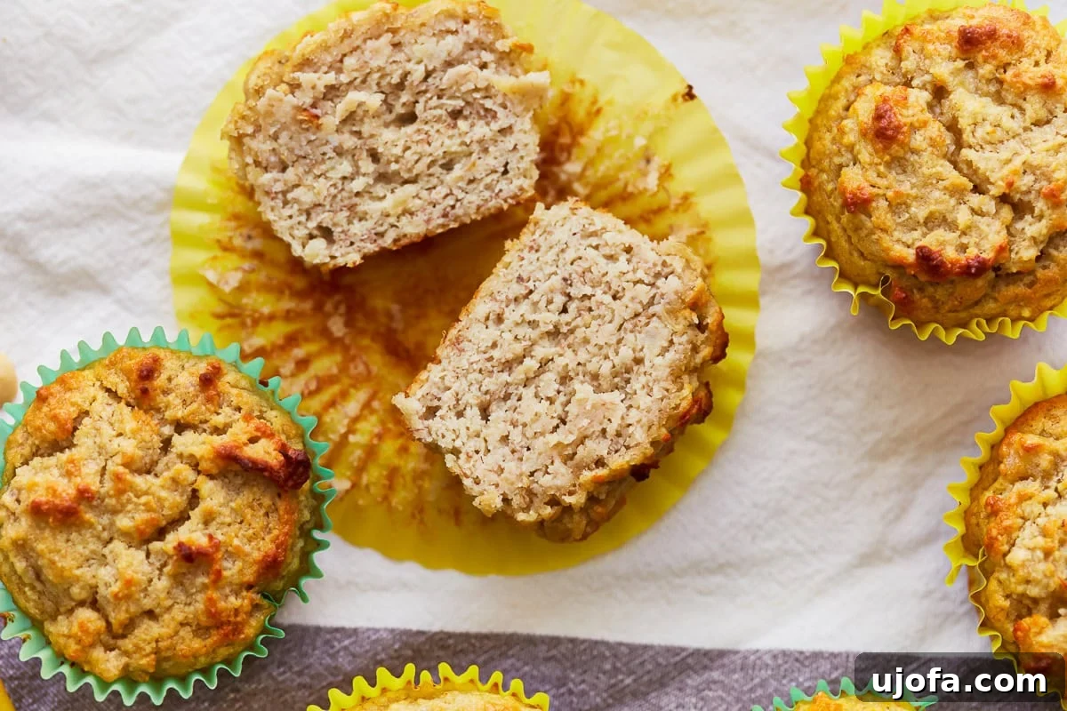 Almond flour banana muffins on a table, with one cut in half to show the moist interior.