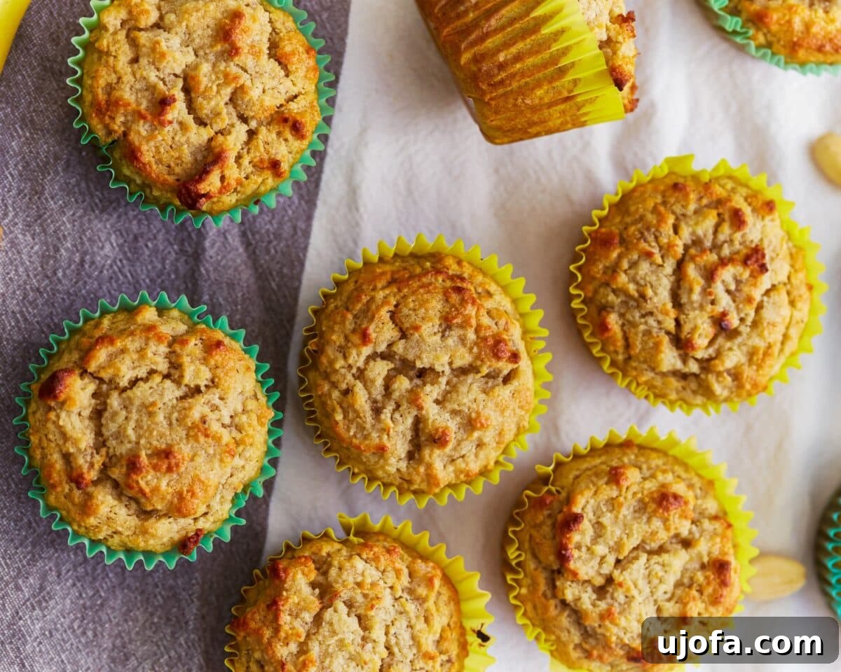 Batch of almond flour banana muffins in yellow and green paper liners, golden brown on top, arranged on a cloth napkin.