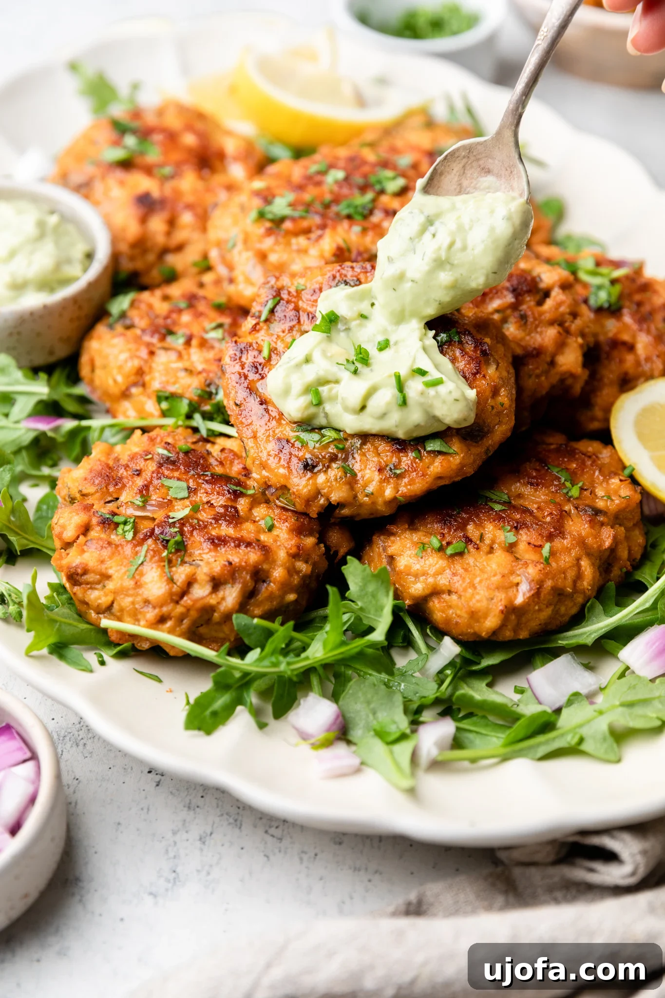 Keto Southwest Salmon Cakes with Cool Avocado Crema 2 Southwest salmon patties with avocado ranch aioli over greens on a white platter