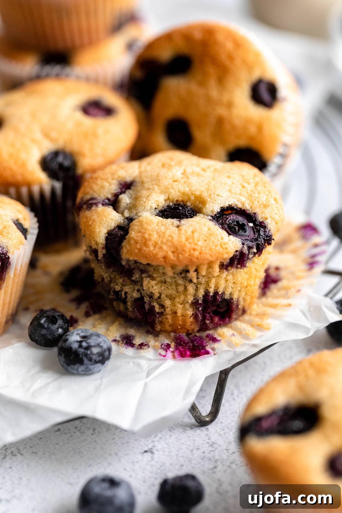 an unwrapped almond flour blueberry muffin on a plate, with a bite taken out, showing the moist crumb and baked blueberries.