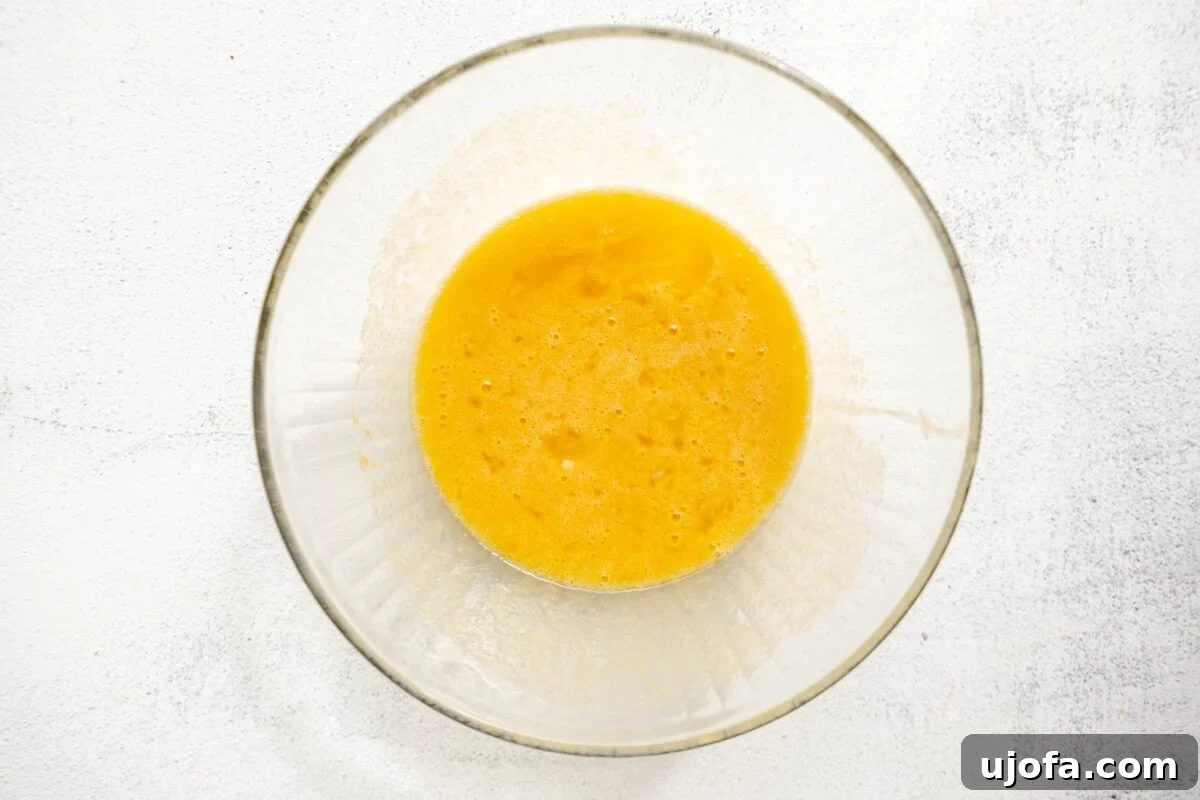 A clear glass bowl containing a mixture of wet ingredients for almond flour blueberry muffins, with a smooth golden color against a light countertop background.