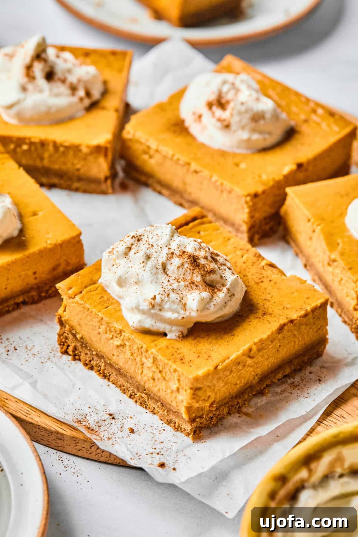 Easy Protein-Packed Pumpkin Cheesecake Bars 2 pumpkin cheesecake bars on parchment with whipped cream