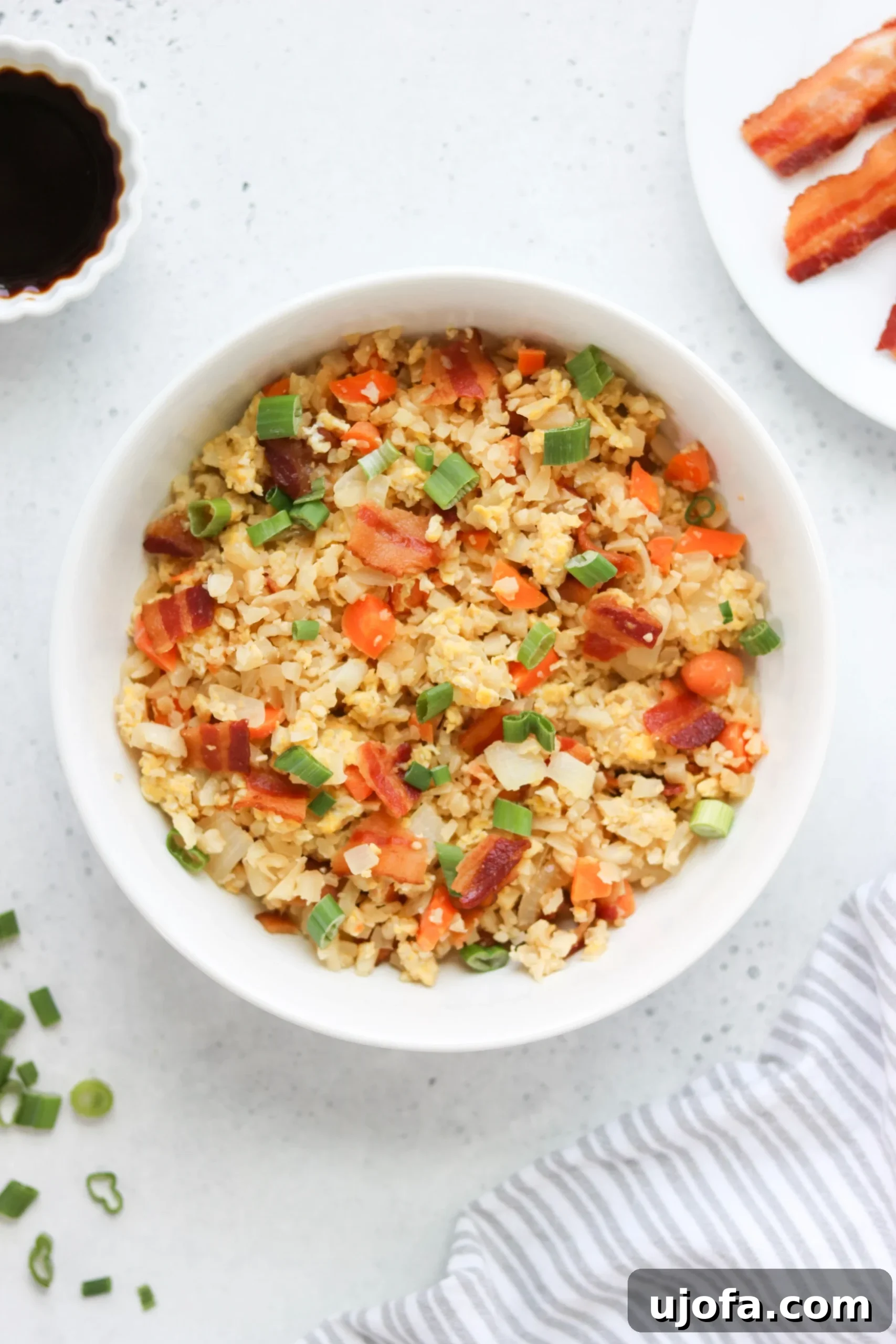 A vibrant bowl of Paleo Breakfast Fried Rice with crispy bacon bits, scrambled eggs, and green onions, showcasing a delicious and healthy meal.