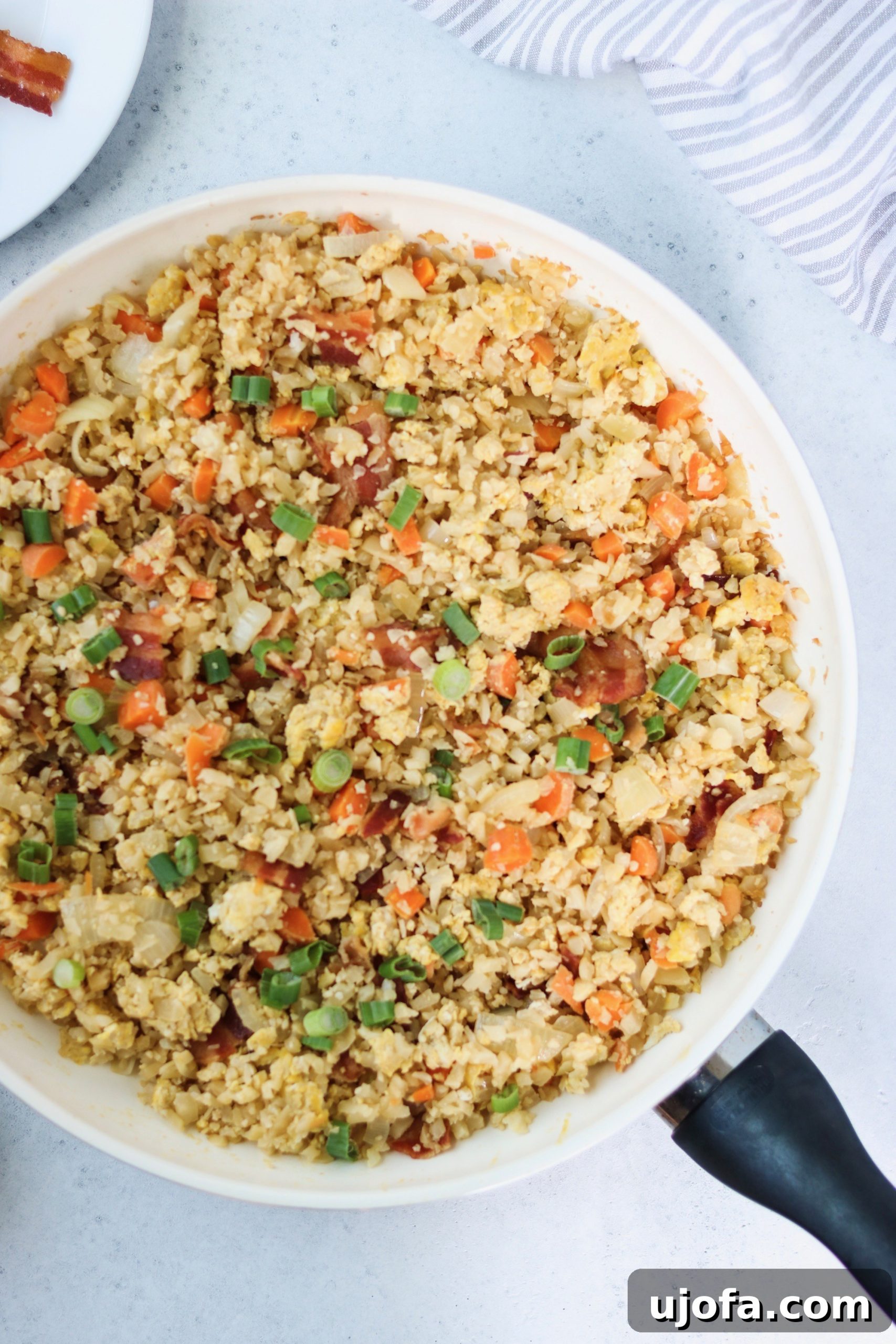 Ingredients for Paleo Breakfast Fried Rice laid out on a cutting board, including cauliflower rice, bacon, eggs, onions, carrots, and green onions.
