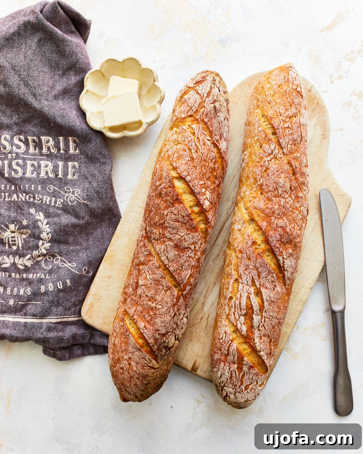 overhead view of 2 gluten free baguettes on a wooden cutting board with butter.