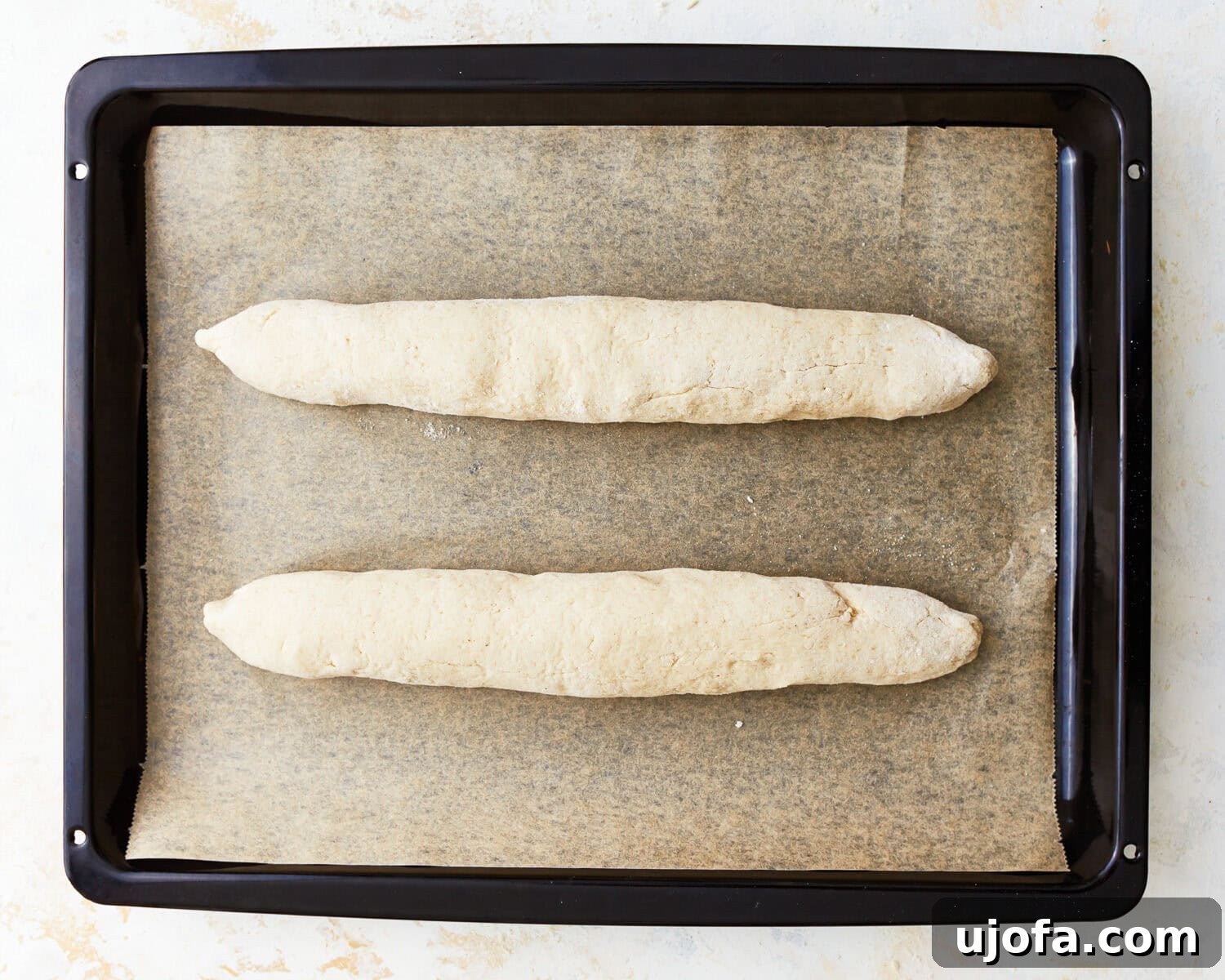 Gluten-free baguette dough shaped into logs on a parchment lined baking sheet.
