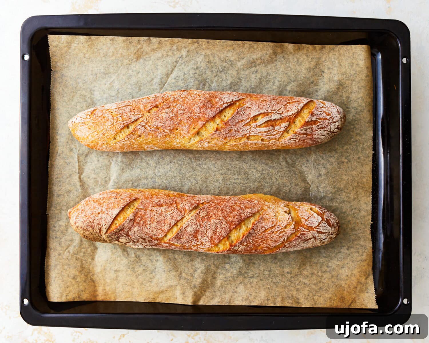 Two gluten-free baguettes on a parchment lined baking sheet.