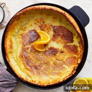 overhead view of a gluten-free dutch baby in a pan with an orange slice. The pancake is golden brown and perfectly puffed, served with fresh citrus.