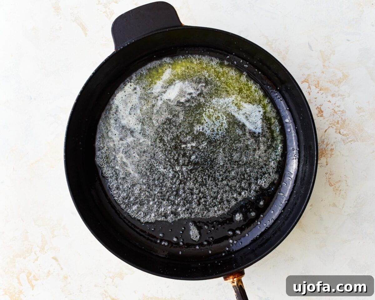 Foamy melted butter coating the bottom of a cast-iron skillet, creating a glistening, golden base before the batter is added.