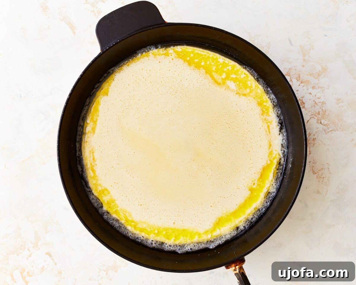 Raw gluten-free Dutch baby batter freshly poured over the melted butter in a hot cast-iron skillet, ready for baking.