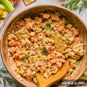 Buffalo tuna salad in a pink bowl with a wooden spoon surrounded by crackers and ingredients