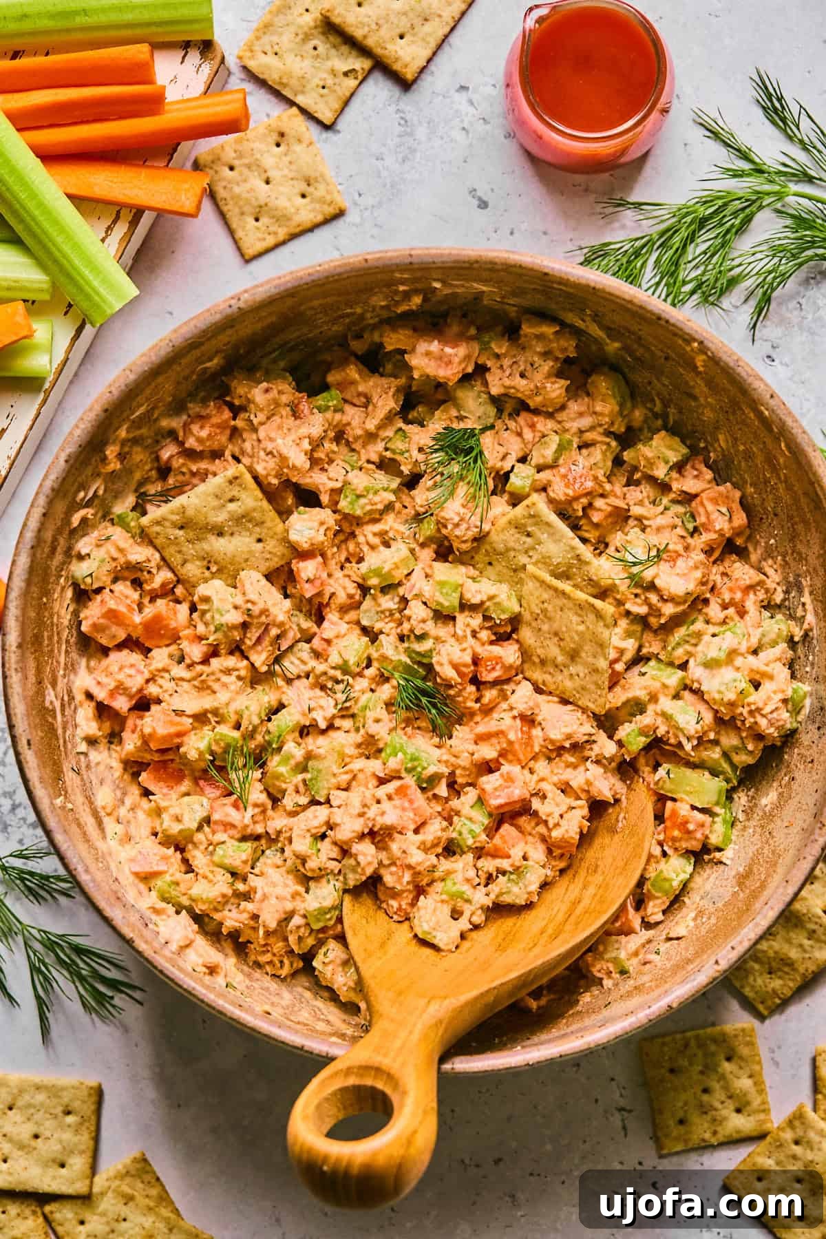 A bowl of buffalo tuna salad surrounded by various crackers and fresh dill, showcasing its creamy texture