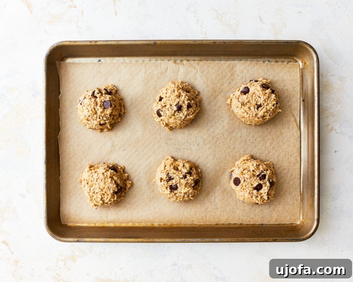 Wholesome Banana Oat Cookies 8 Six scoops of banana oatmeal cookie dough spaced on a parchment-lined baking tray before baking.