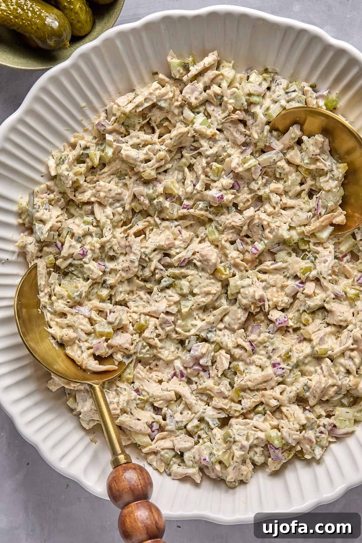 chicken salad with dill pickles in a large bowl with 2 gold spoons.