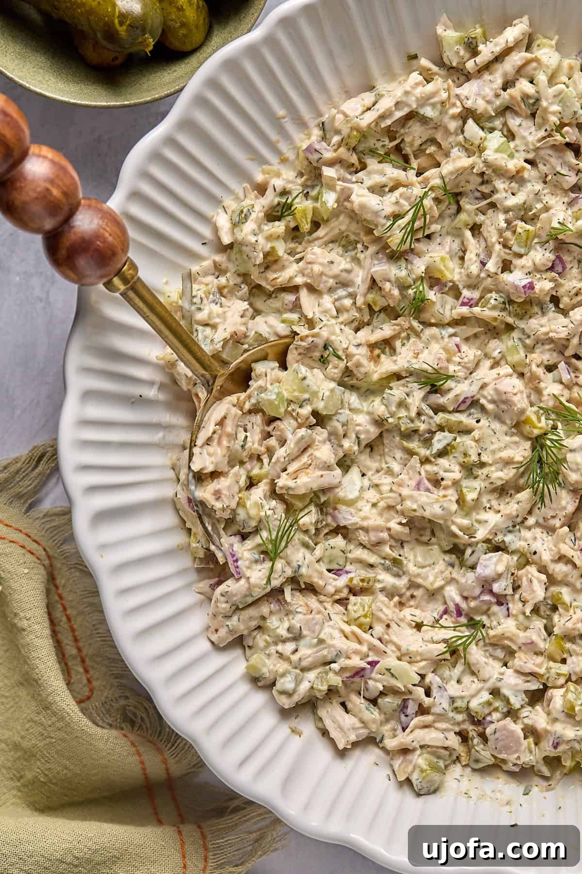 half view of a white bowl of chicken salad with a gold serving spoon