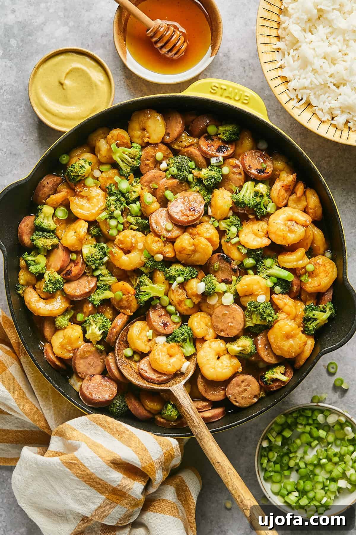 Vibrant hot honey shrimp and sausage stir fry, garnished with green onions, served in a sunny yellow Staub skillet, ready to be enjoyed.