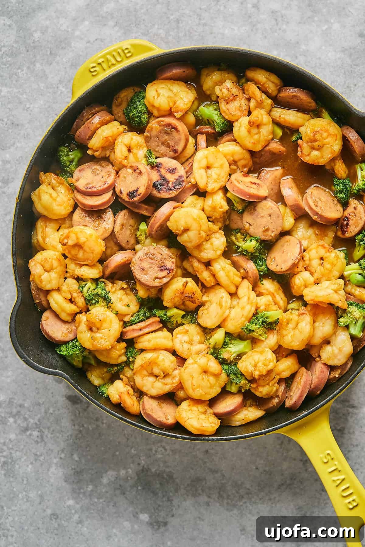 Final hot honey shrimp and sausage stir fry with broccoli in a yellow Staub pan, glistening with sauce.
