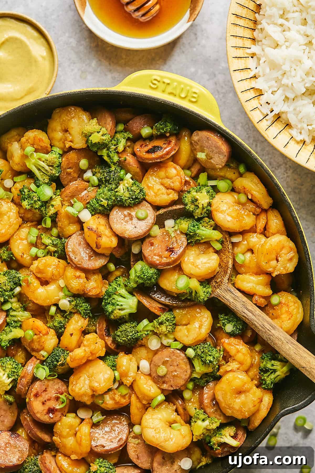 Close-up of hot honey shrimp and sausage stir fry with broccoli, ready to eat, in a yellow skillet with a wooden spoon.