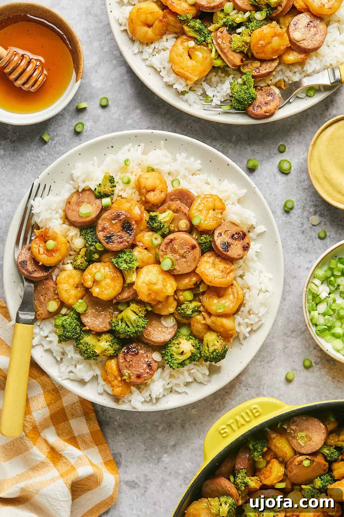 Two plates of hot honey shrimp and sausage stir fry served over white rice, garnished with green onions.