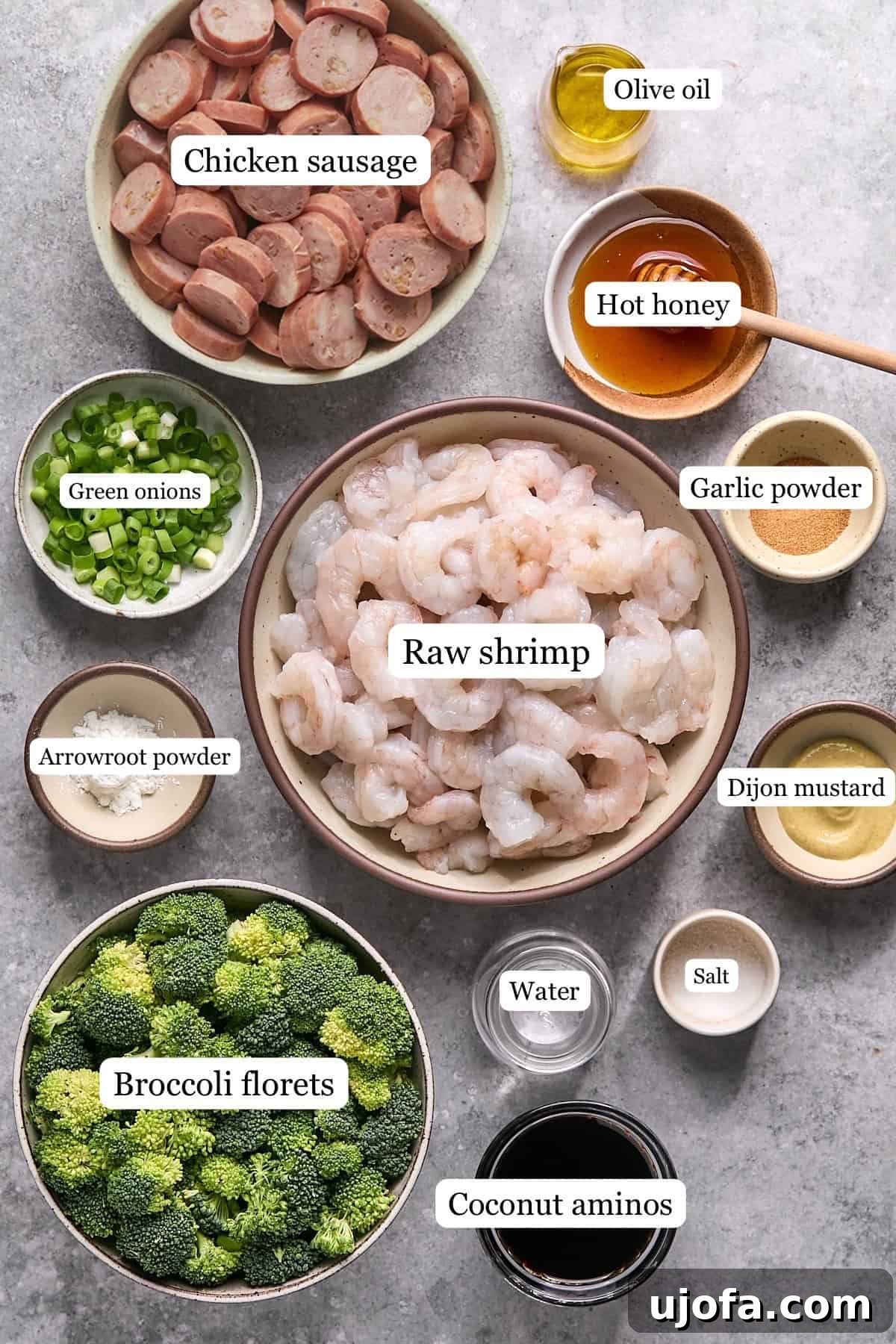 Arrangement of stir-fry ingredients in separate bowls: olive oil, sliced chicken sausage, raw shrimp, fresh broccoli florets, water, and sliced green onions.
